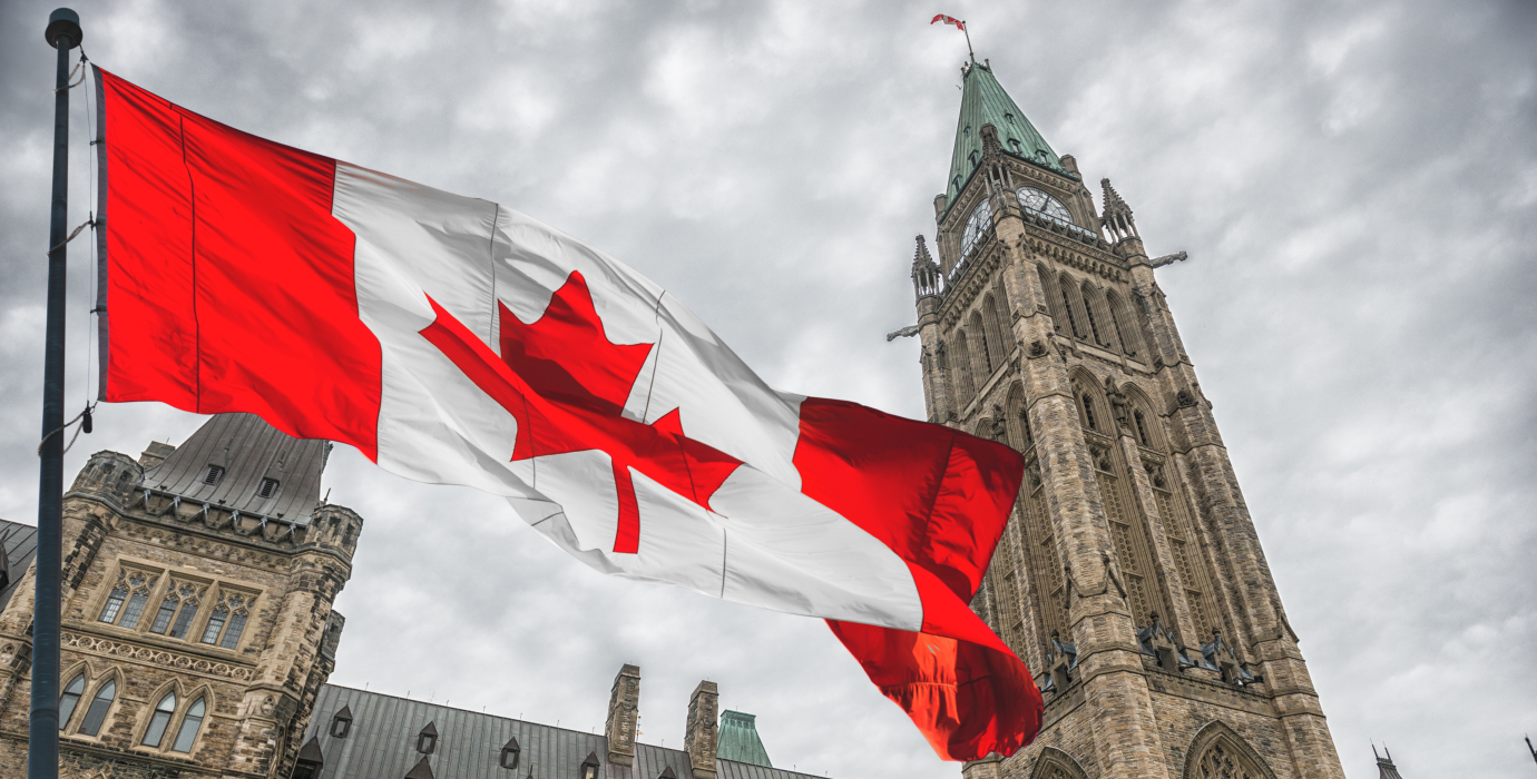 Canadian flag flying with the parliament buildings in Ottawa in the background. 