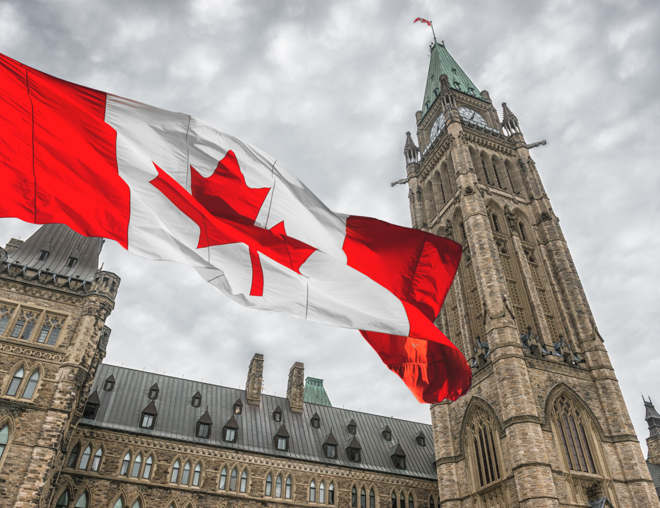 Canadian flag flying with the parliament buildings in Ottawa in the background. 