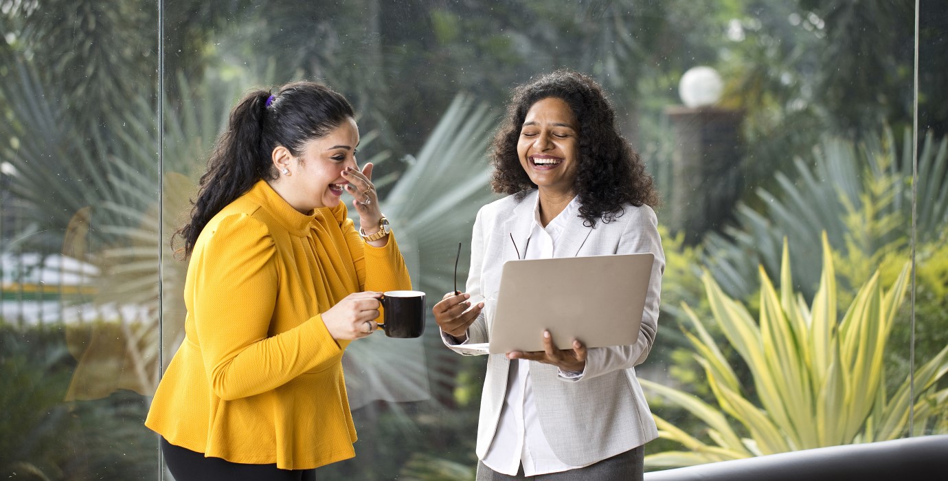 Two coworkers laughing while looking at a laptop. 