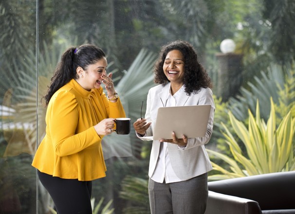 Two coworkers laughing while looking at a laptop. 