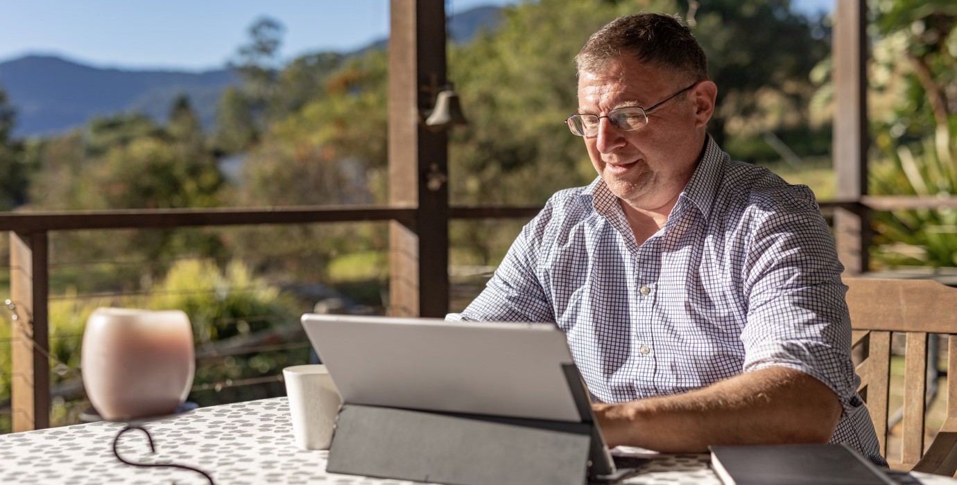 Person working on laptop on their porch in a rural setting.