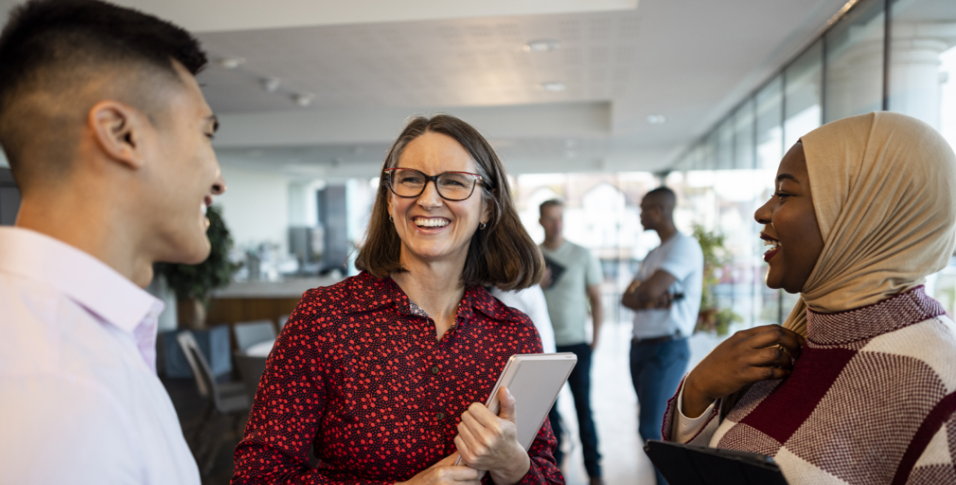 3 people happily talking while standing in office.