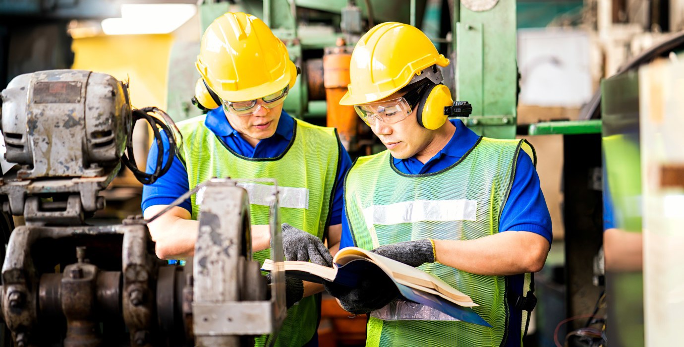 2 workers looking at a manual for a machine in their shop.