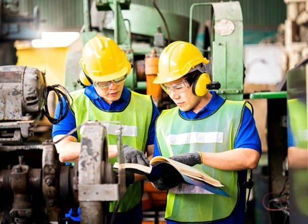 2 workers looking at a manual for a machine in their shop. 